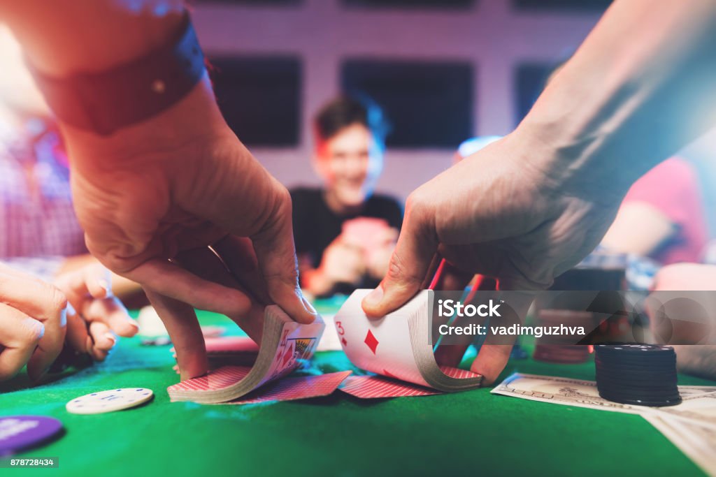 Young people play poker at the table. Young people play poker at the table. On the table they have glasses with alcoholic beverages, mobile phones and chips for the game. They have fun playing a game. Poker - Card Game Stock Photo