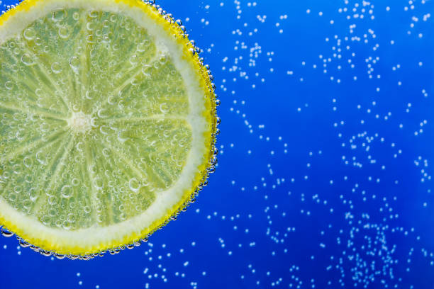 slice of lemon in the blue water with bubbles - adhering imagens e fotografias de stock