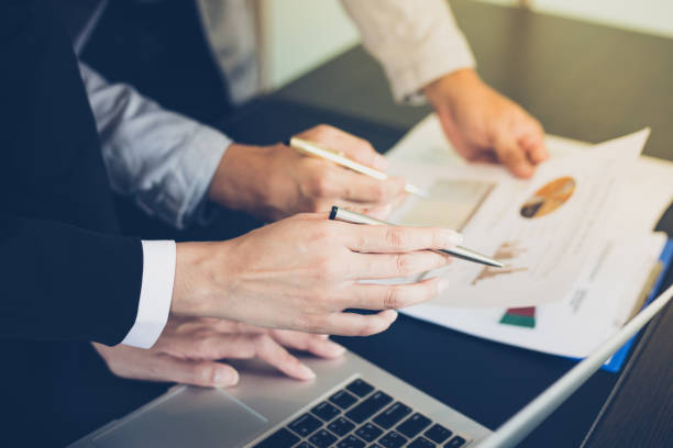 istock Asian businesswomen holding a pen and analysis documents on office table with laptop computer and graph financial diagram working in the background 878795582