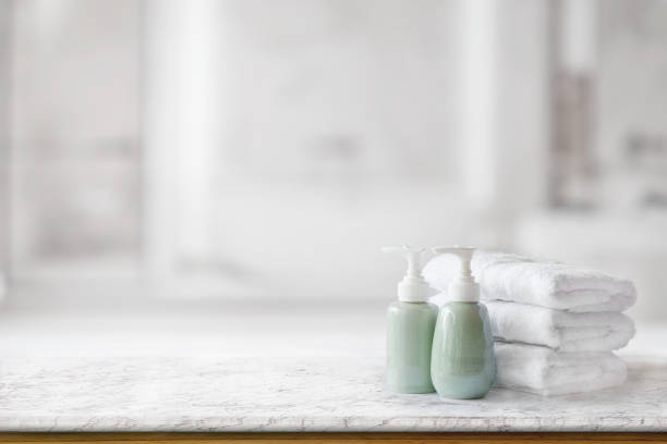 istock Ceramic soap green bottles and white cotton towels on a marble counter table inside a bright bathroom background. 878803682