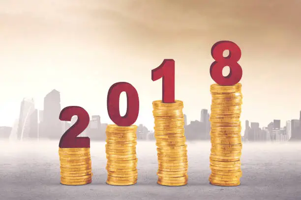 Image of numbers 2018 above pile of gold coins shaped growth graph with skyscraper background