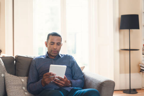 istock Man relaxing with digital tablet on sofa at home 878830184