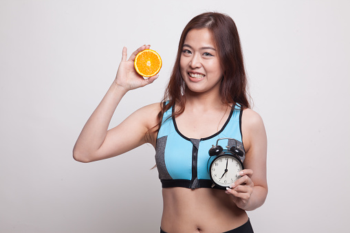 Beautiful Asian healthy girl with orange and clock on white background