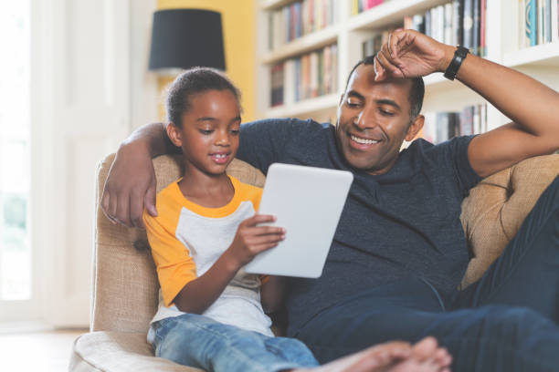 istock Father and daughter sitting on sofa with tablet 878830982