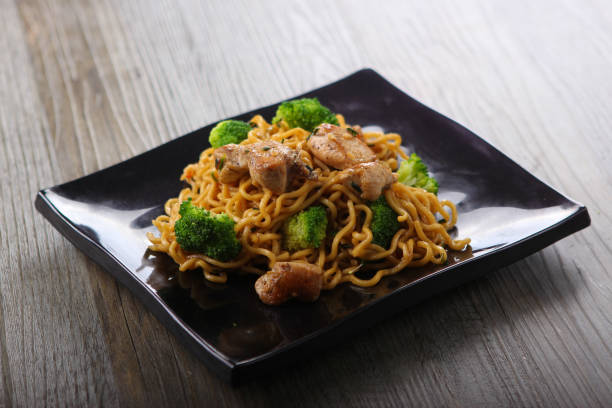 Chicken and broccoli noodles with sweet soy sauce on black plate on wooden background