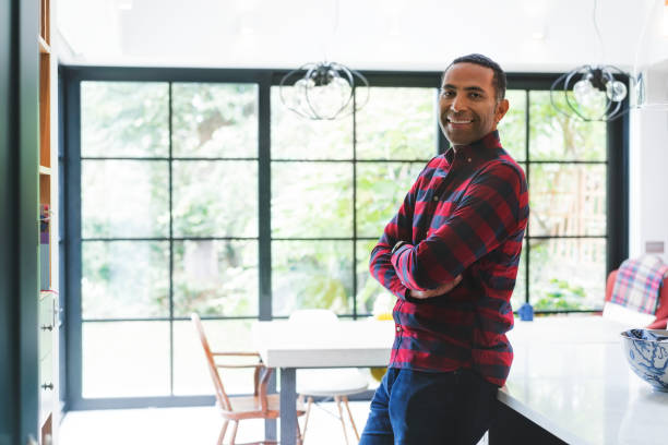 istock Smiling man with arms crossed against window 878840990
