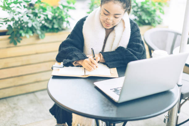 istock young woman making notes with laptop in sidewalk cafe 878859858