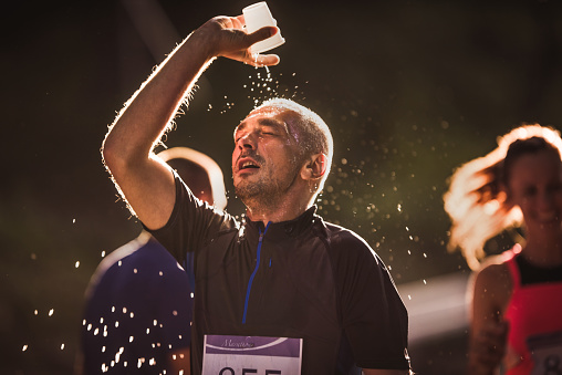 Tired male runner refreshing himself with fresh water during a marathon in nature.