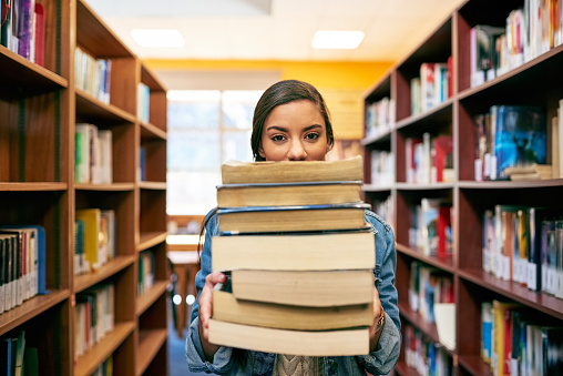 Portrait of a university student holding a pile of books in the library at campus