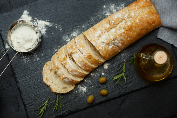 istock Ciabatta bread sliced, olives, olive oil and flour on a black stone surface 878871582