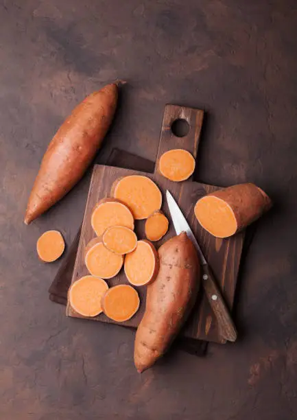 Photo of Sweet potato on wooden kitchen board from above.