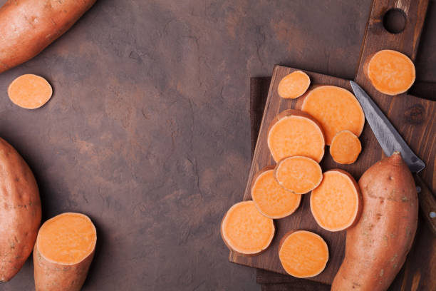 istock Raw sweet potato whole and chopped on kitchen table top view. Copy space for text. 878879452