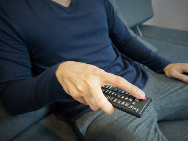 istock Pressing TV remote channel, sitting on sofa 878882646