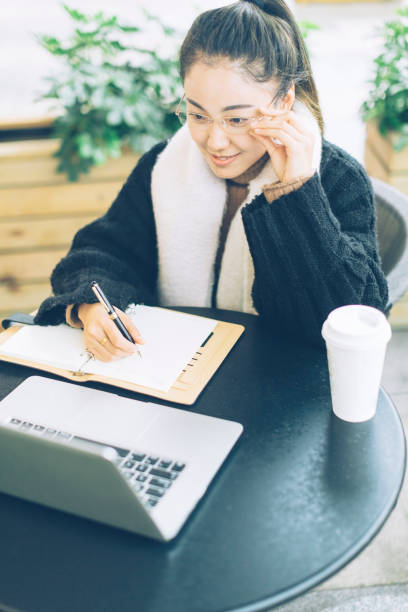 istock young woman making notes with laptop in sidewalk cafe 878885156