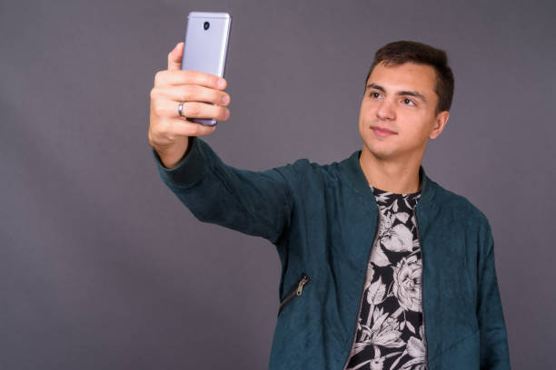 Young handsome man wearing floral patterned shirt and blue jacket against gray background