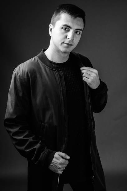 istock Young handsome man wearing jacket against gray background in black and white 878894328