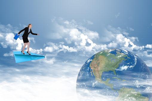 Businesswoman flying on paper airplane towards planet earth, globalization concept
