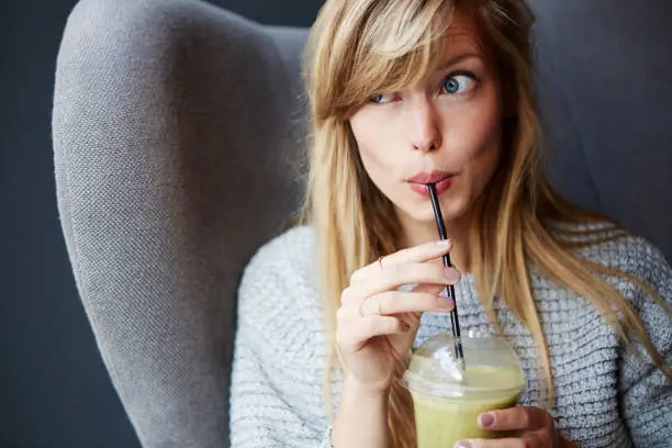 Beautiful young blond woman with smoothie in cafe, looking away