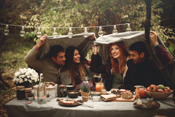 I think it's raining... Happy friends covered with blanket having fun. fall picnic table stock pictures, royalty-free photos & images