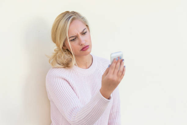 istock Sad young woman using phone on blank wall 878918880