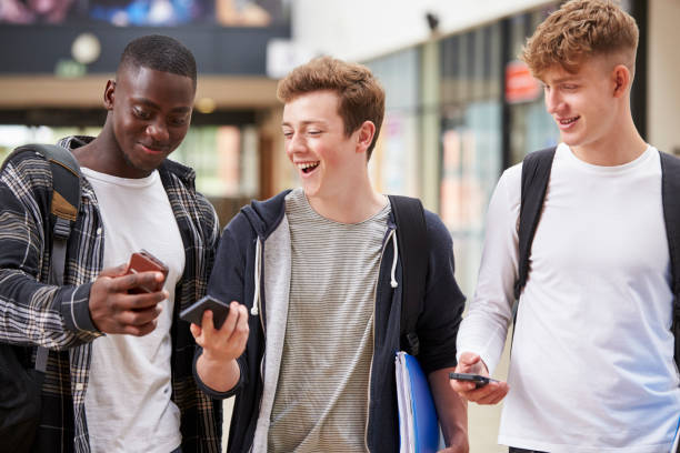trois étudiants du collège de mâle lire message texte sur téléphone mobile - three boys photos et images de collection