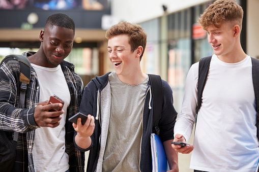 Three Male College Students Reading Text Message On Mobile Phone