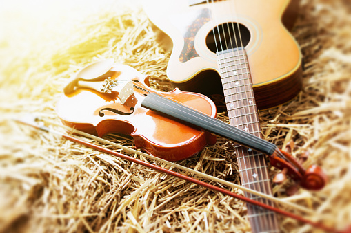 A fiddle and an acoustic guitar sit on straw, brightly lit by the sun, ready to make some music.