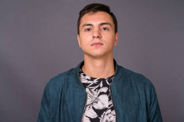 istock Young handsome man wearing floral patterned shirt and blue jacket against gray background 878934844
