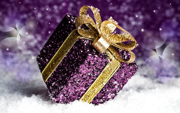 istock purple shiny gift with a gold bow, on a snowy background 878939420