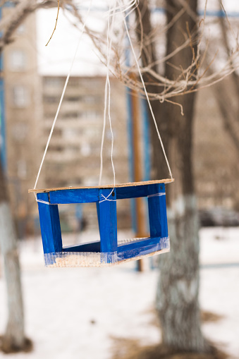 Hanging blue bird feeder, made of wood. Handmade. On the blurred snowy background.