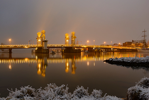 Evening on the skyline of the city of Kampen in Overijssel, The Netherlands. The lights of the city are reflected in the calm water while the sky has turned blue right after sunset. There is snow on the pier in the foreground.