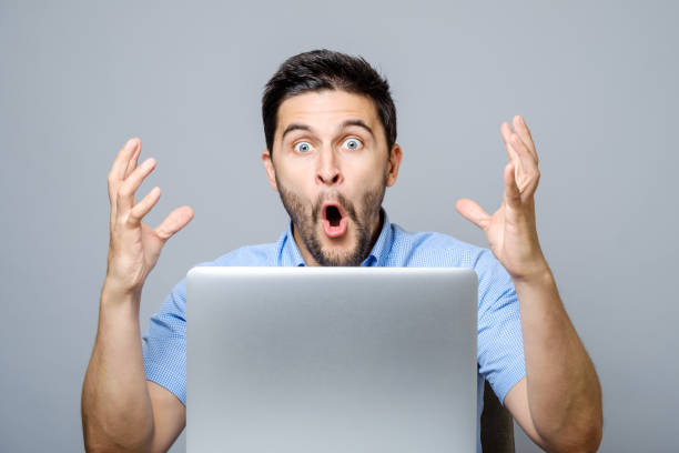 istock Portrait of amazed man with laptop computer over gray background 878994292