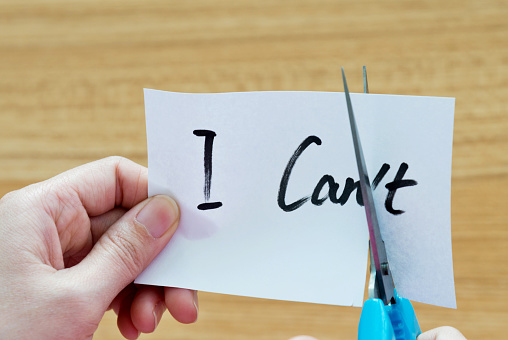 Woman hand holding scissors cutting word 'I can't'