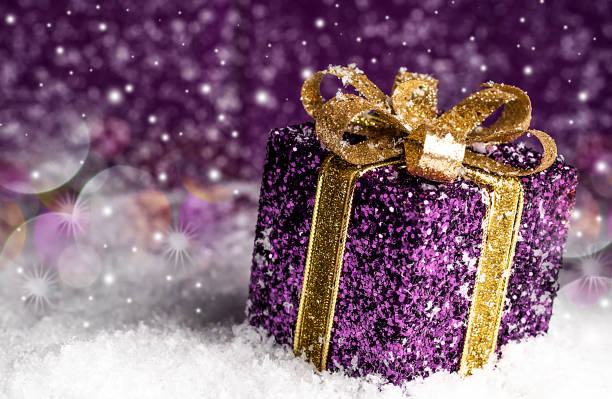 istock purple shiny gift with a gold bow, on a snowy background 879006890