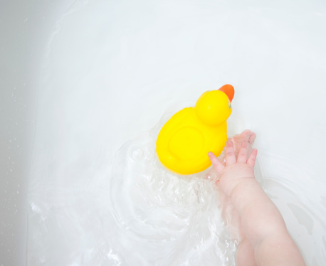 Baby (9-12 months) sitting in bathtub with rubber duck