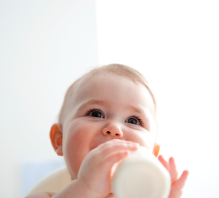 Baby girl (9-12 months) drinking from bottle, smiling, portrait