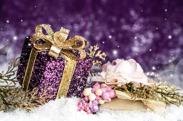 istock purple shiny gift with a gold bow, on a snowy background 879040904