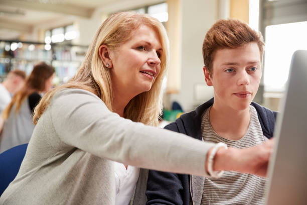 istock Teacher With Male Student Working On Computer In College Library 879041096