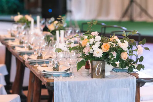 Photo of rest, food, party concept. wooden table numbered six prepared for holiday dinner and decorated with amazing grand bouquet of marvelous roses of white and orange color