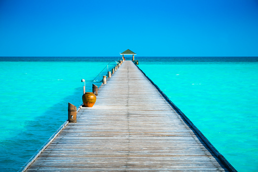 Jetty at tropical paradise beach at Dhiffushi Holiday island at South Ari atoll, Maldives. Beautiful turquoise Indian ocean sea with white sand. Luxury travel holidays background. Property released.