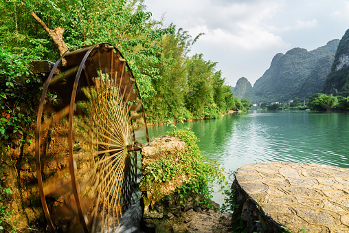 Moving water wheel (noria) on the Yulong River in Yangshuo County of Guilin, China. Beautiful karst towers are visible in background. Yangshuo County is a popular tourist destination of Asia.