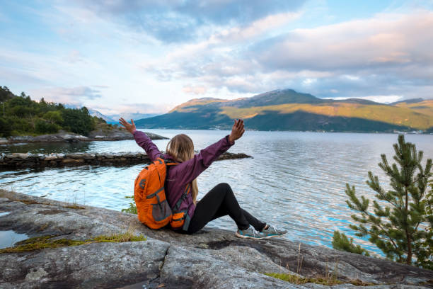 istock Young woman with backpack standing on fjord coast 879058698