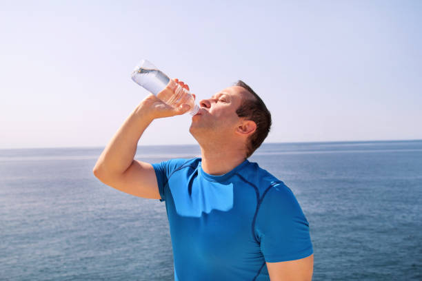 istock An athlete making a break during training, drinking fresh clean water from a bottle, rests and enjoys the clean air, with a beautiful blue sky and the sea in the background. Healthy lifestyle concept. 879089098