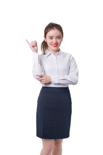 A young Caucasian brunette businesswoman in a white shirt points her finger at a copy space for advertising isolated on a gray studio background.