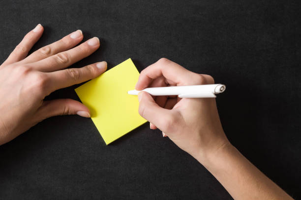 Woman writing in the yellow sticky notes. Working on the table. Empty place for a important ideas, plans, memories, messages, compliments or other text with positive mood. Reminder concept. stock photo