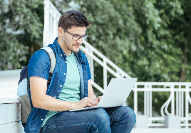 istock Young man sitting with laptop outside the office 879120242