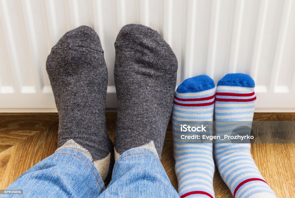 Feet in woolen winter socks warm their feet and relaxing near heating radiator at home. Adult Stock Photo