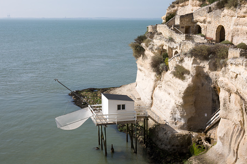 View from the Gironde estuary with the limestone cliff of the village of Meschers sur Gironde and its troglodytic houses and traditionnal typical wooden fisherman cabins