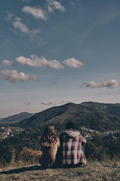 Rear view of young couple admiring the view while sitting on the mountain top