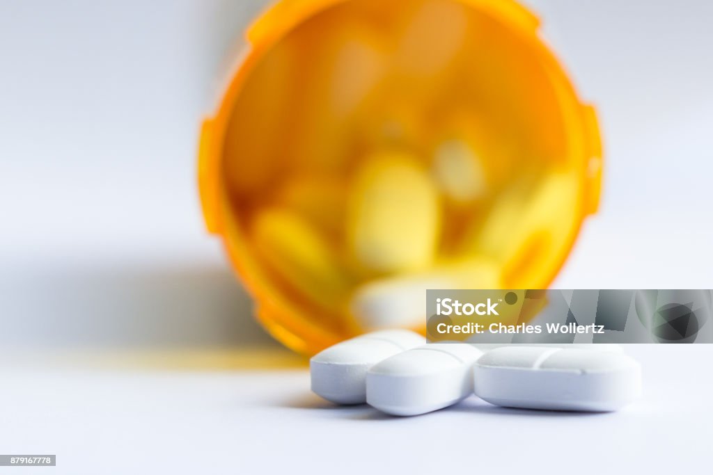 Opioid pain killers close up of a group of white tablets with an out of focus prescription bottle in the background Opioid Stock Photo